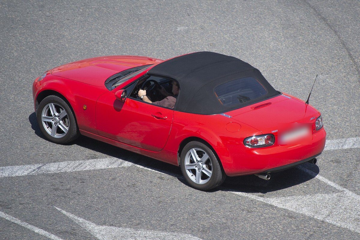 Mazda MX-5 de tercera generación rojo con la capota de lona negra puesta, visto desde arriba en una calle de Valencia.