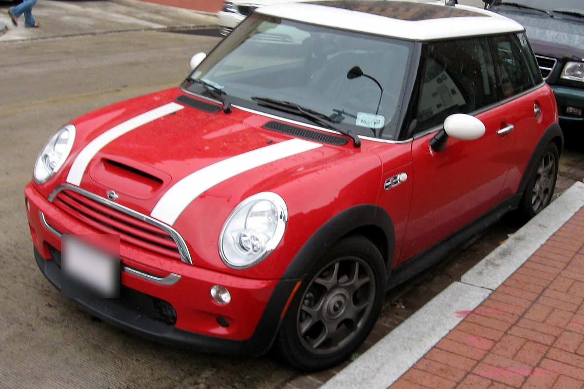 MINI Cooper S de primera generación rojo con techo blanco y bandas blancas en el capó, aparcado junto a una acera.