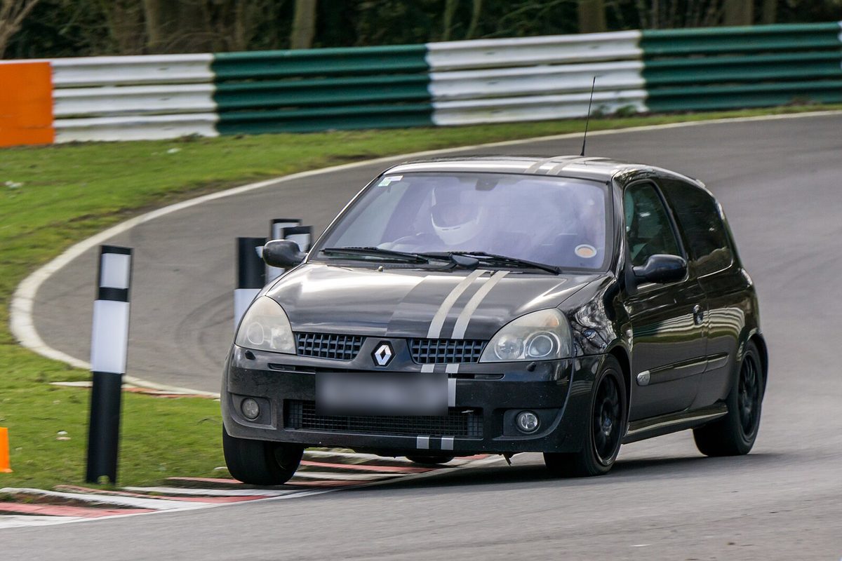 Renault Clio Sport 182 negro con bandas grises en el capó, rodando en un circuito.