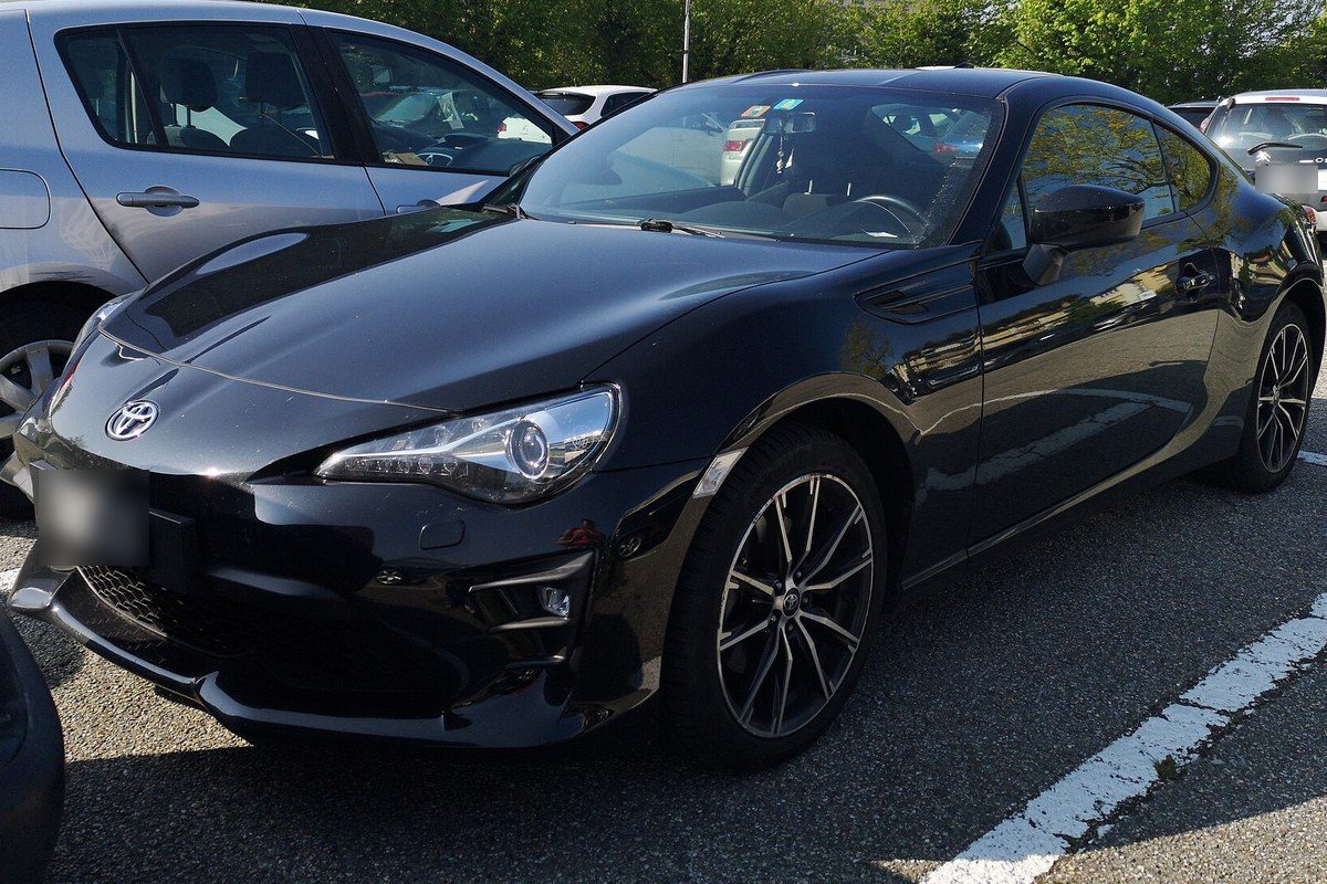 Toyota GT86 negro con faros LED, posterior al restyling, aparcado en un aparcamiento entre otros coches.